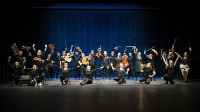 SibA folk big band is posing on the floor of black box concert hall. They have placed their instruments up and everyone wears a big smile