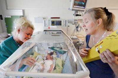 Music practitioner Uli Kontu-Korhonen performs by singing and playing the guitar to an infant and a nurse in a hospital setting.