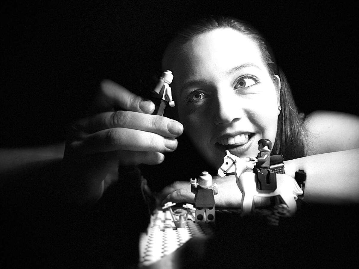 A young woman plays with lego figurines in a black and white picture
