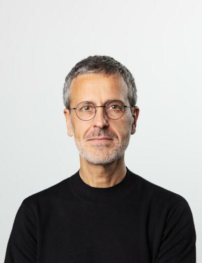 Portrait of Alex Arteaga with black sweater and glasses against a grey background.