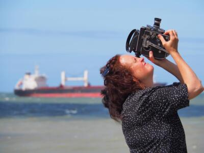 Woman by the sea, aiming at the sky with a film camera.