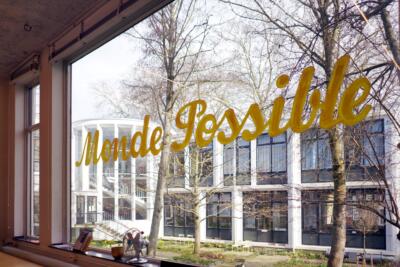 White recidency building through a window. The window has "Monde Possible" text written on it.